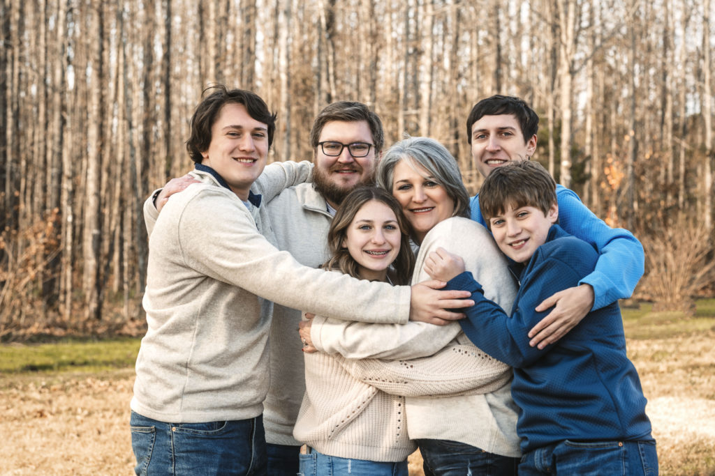 family hugging in front of trees wearing sweaters. The power of family photos Nelly Hernandez Photography