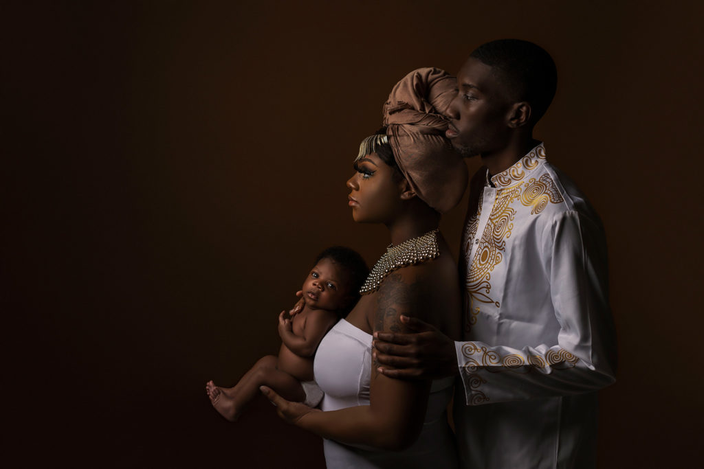 family of three posing in front of brown background. The power of family photos Nelly Hernandez Photography