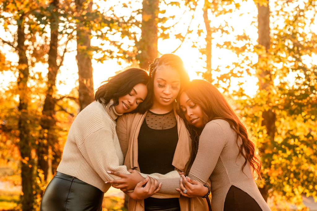 three black American women holding and embracing each other in front of trees. The power of family photos Nelly Hernandez Photography