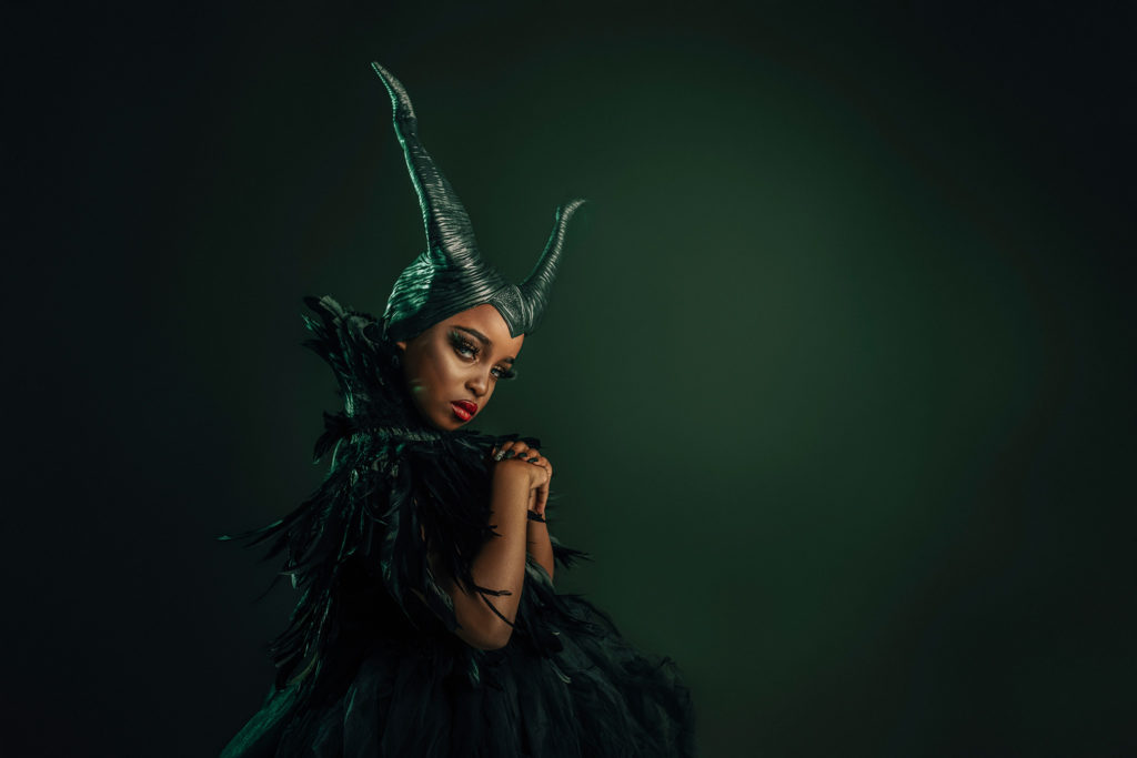 green background with child dressed up as Maleficent, halloween costume 