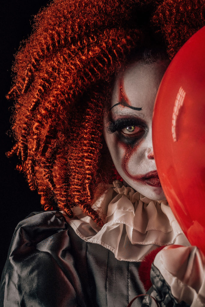 little girl wearing costume of scary clown and holding balloon